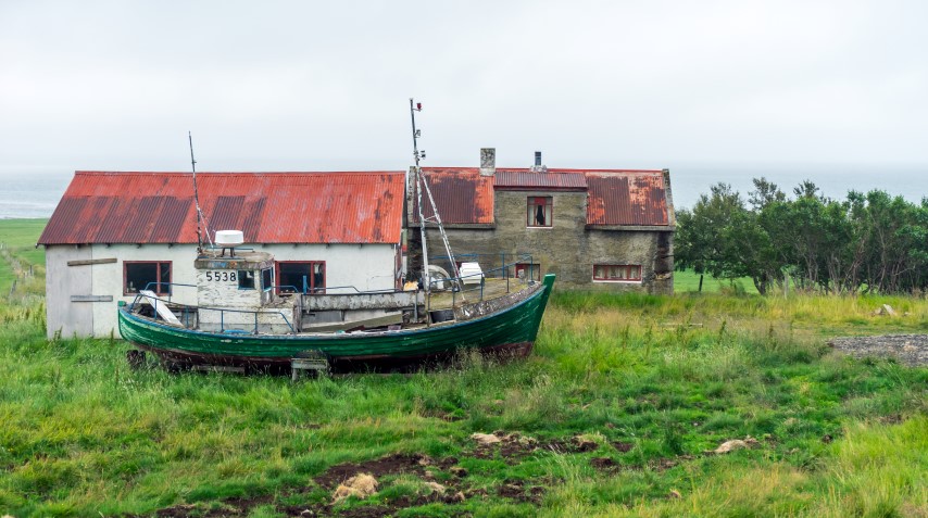 Verlassenes Haus und altes Fischerbootwrack im Freien in der isländischen Wildnis in den Westfjorden.