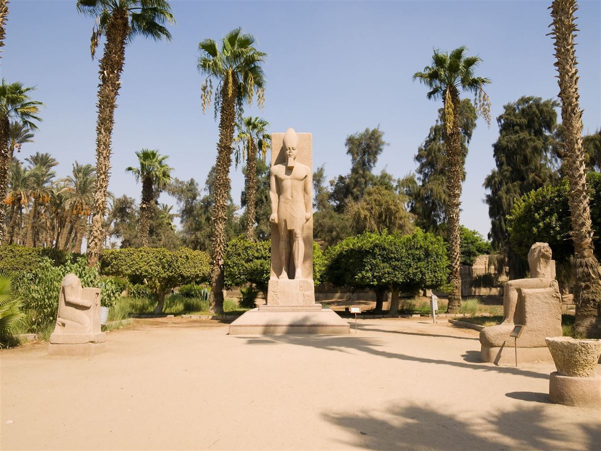 Open-air archaeological setting at Memphis Museum in Mit Rahina with monumental royal sculpture and palm trees