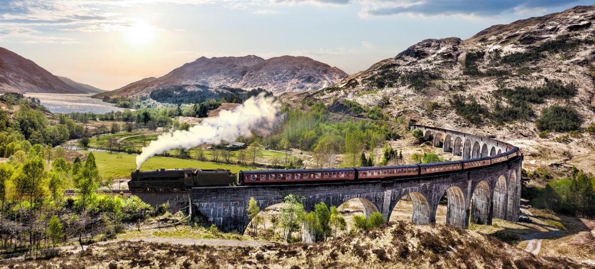Glenfinnan Railway Viaduct mit dem Jacobite-Dampfzug bei Sonnenuntergang über dem See